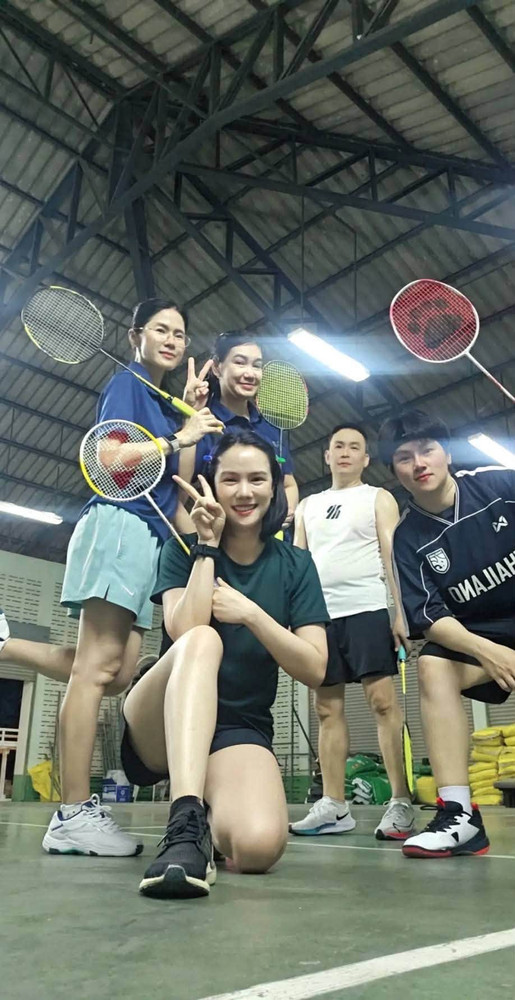 หญิงกับเพื่อน 5 คนในสนามแบดมินตันในร่ม ถือแร็กเก็ตโพสท่าชูสองนิ้วด้วยกัน จากผลงาน ID 076